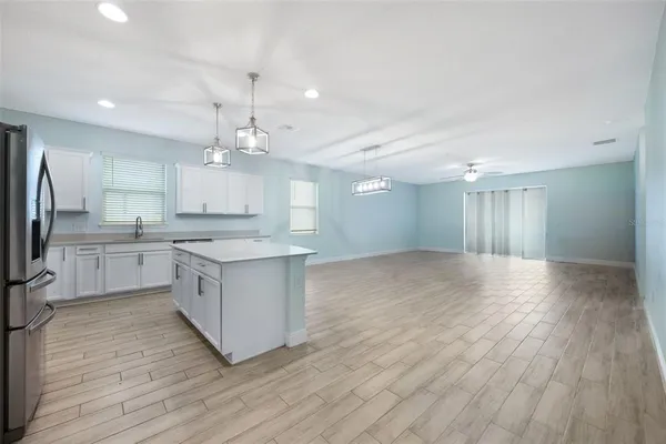 a large kitchen with kitchen island a stove a sink dishwasher a refrigerator and white cabinets with wooden floor