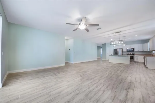 a view of an empty room and kitchen view with wooden floor