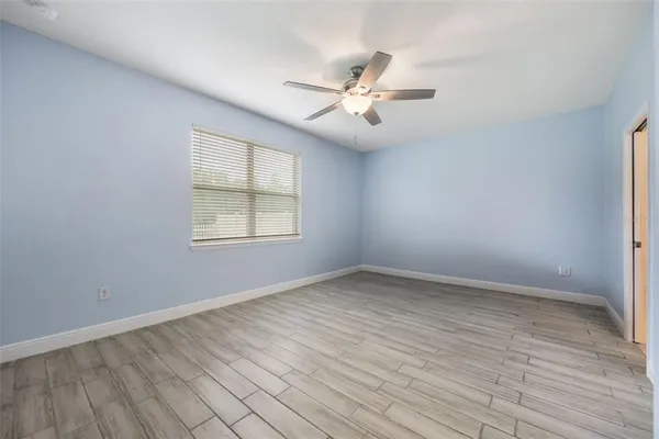 an empty room with wooden floor fan and windows