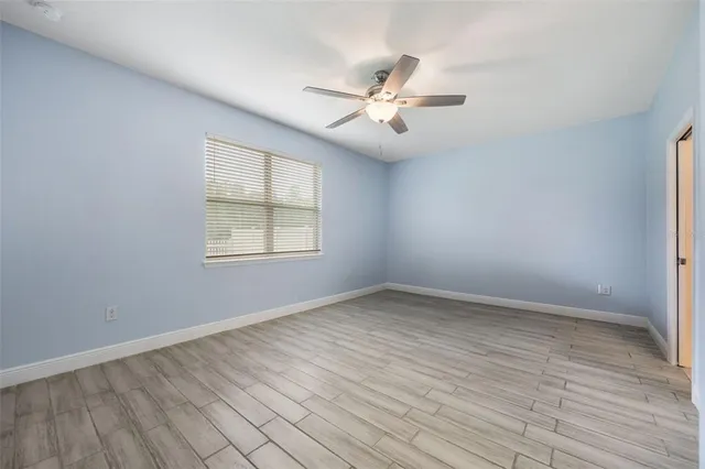an empty room with wooden floor fan and windows