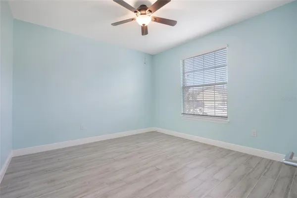 an empty room with wooden floor chandelier fan and windows