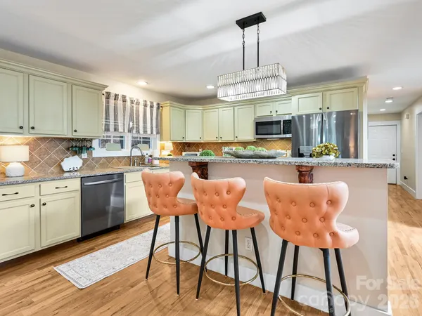 a kitchen with stainless steel appliances granite countertop a stove top oven a refrigerator and chairs