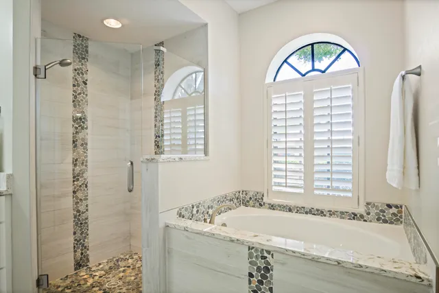 a bathroom with a granite countertop sink a mirror a bathtub and next to a window