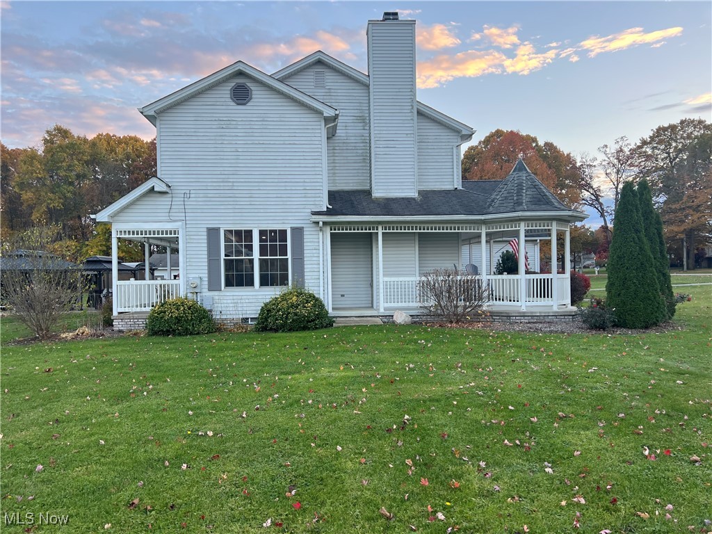 Back of property featuring a lawn, a chimney, a porch, and roof with shingles