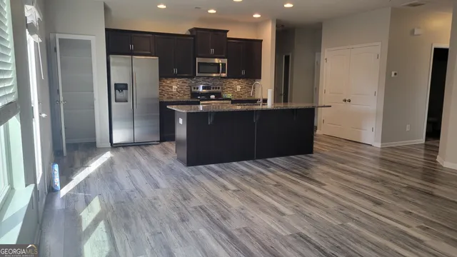 a kitchen with stainless steel appliances kitchen island granite countertop wooden floors a refrigerator and a sink