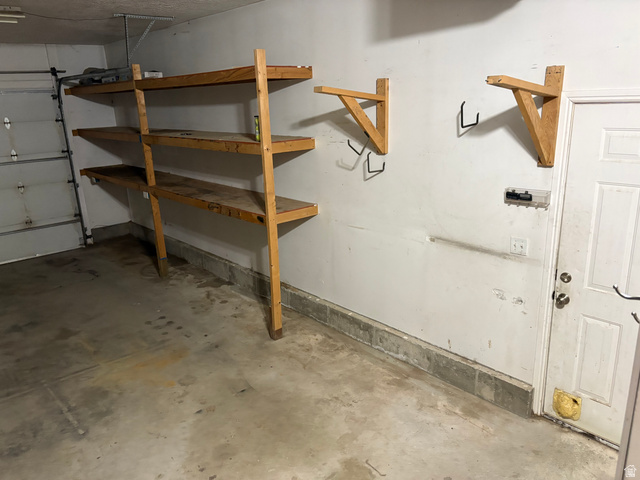 587 West 2400 South Perry, UT 84302 - Photo 19 of 46 Garage area featuring built-in wooden shelving units, additional wall-mounted storage brackets, a concrete floor, and a white access door