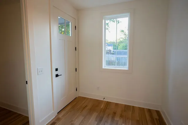 a view of an empty room with wooden floor and a window