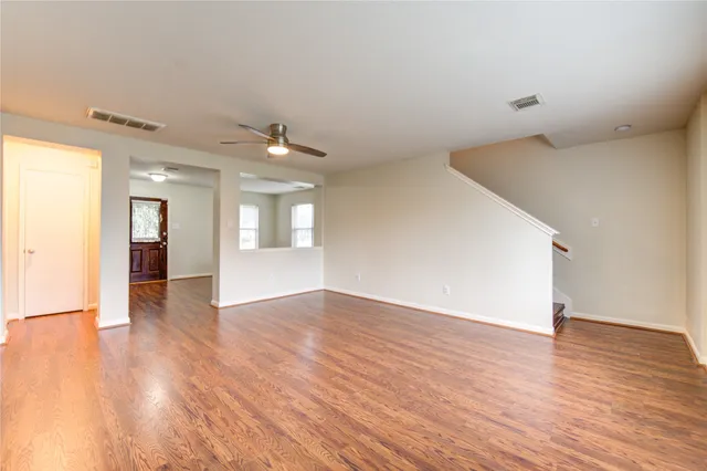 a view of an empty room and kitchen view with wooden floor