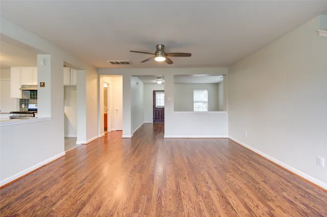 a view of an empty room with wooden floor and a kitchen