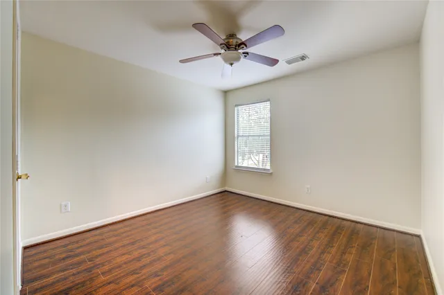 an empty room with wooden floor fan and windows