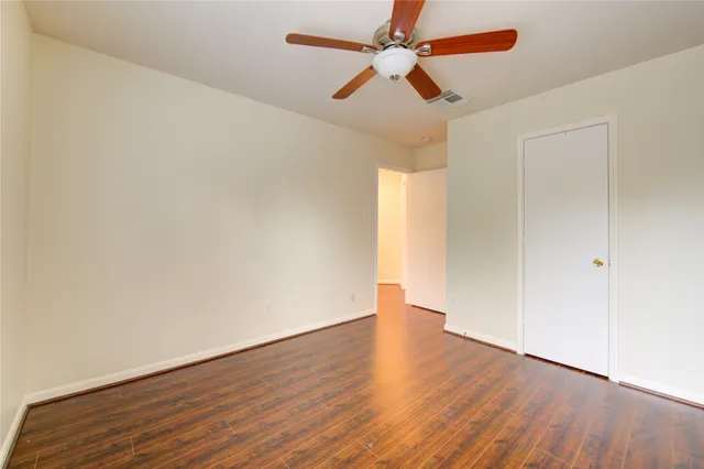 an empty room with wooden floor fan and windows