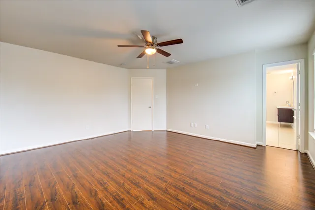 an empty room with wooden floor fan and windows