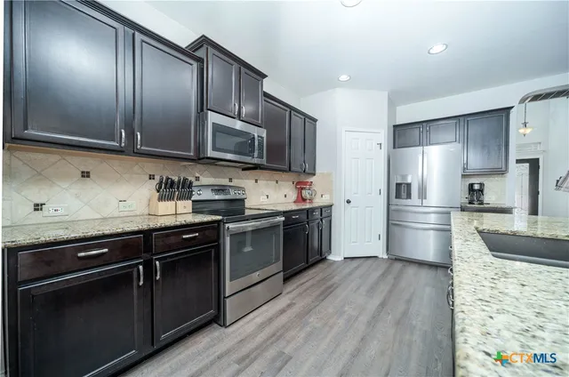 a kitchen with stainless steel appliances kitchen island granite countertop a stove a sink a refrigerator and a wooden cabinets