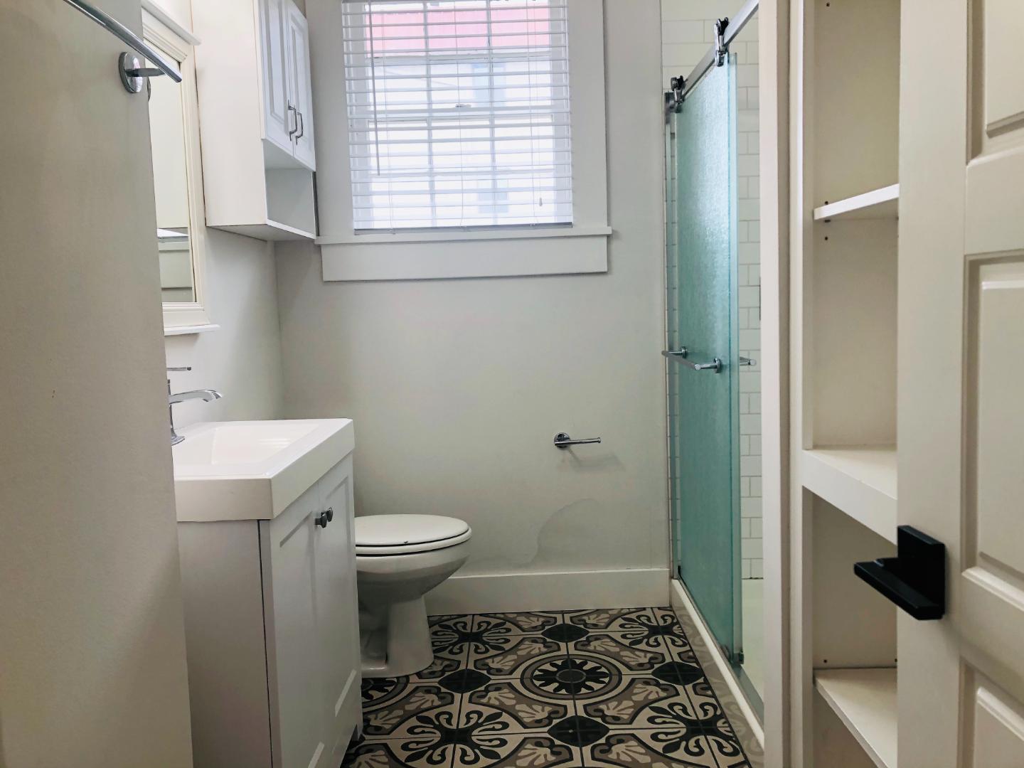 207 West 39th Street, Unit MAIN Austin, TX 78751 - Photo 6 of 7 A well-lit bathroom showcases a contemporary vanity, patterned tile flooring, and a glass-enclosed shower.