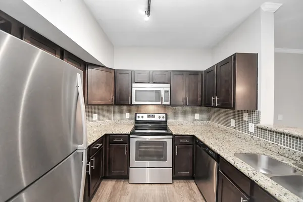 a kitchen with stainless steel appliances kitchen island granite countertop a stove top oven a chimney a dining table and chairs with wooden floor