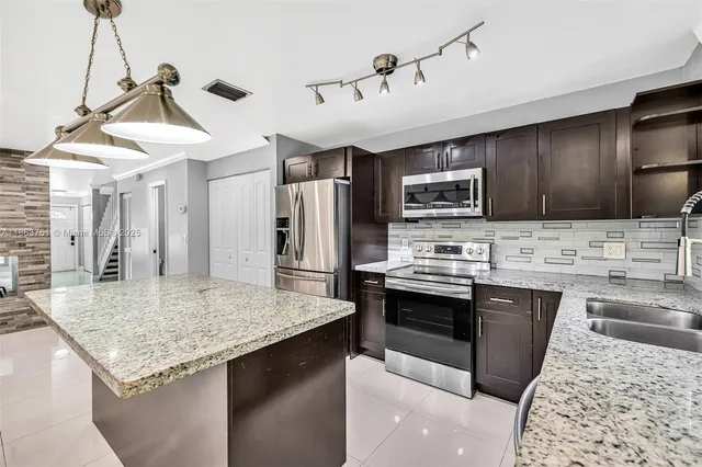 a kitchen with stainless steel appliances kitchen island granite countertop a sink dishwasher stove and refrigerator with wooden floor