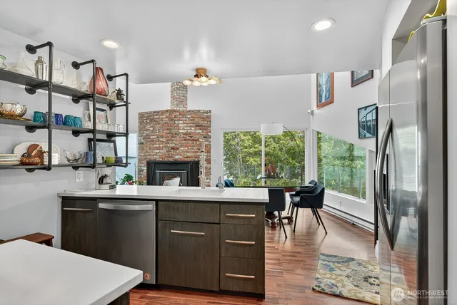 a kitchen with stainless steel appliances granite countertop a refrigerator a sink dishwasher a stove and a dining table with wooden floor