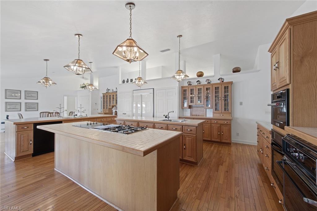 589 Neapolitan Way Naples, FL 34103 - Photo 17 of 27 a kitchen with a stove a chandelier and wooden floor