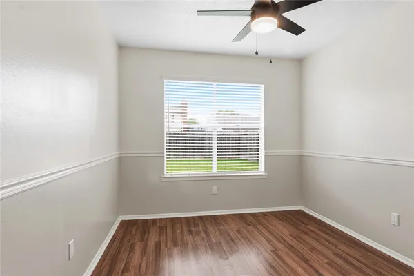 an empty room with wooden floor ceiling fan and windows