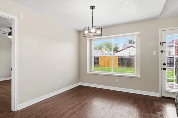 an empty room with wooden floor chandelier and windows