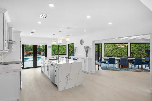 a large kitchen with white cabinets a sink dishwasher a stove and a dining table with wooden floor