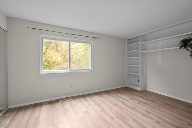 a view of an empty room with a window and wooden floor