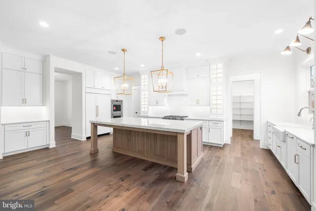 a open kitchen with kitchen island a sink dishwasher a stove and white cabinets with wooden floor