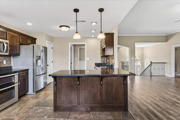 a kitchen with stainless steel appliances kitchen island granite countertop a refrigerator a stove and a sink with wooden floor