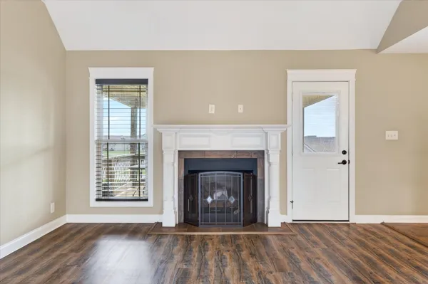a view of an empty room with wooden floor fireplace and a window
