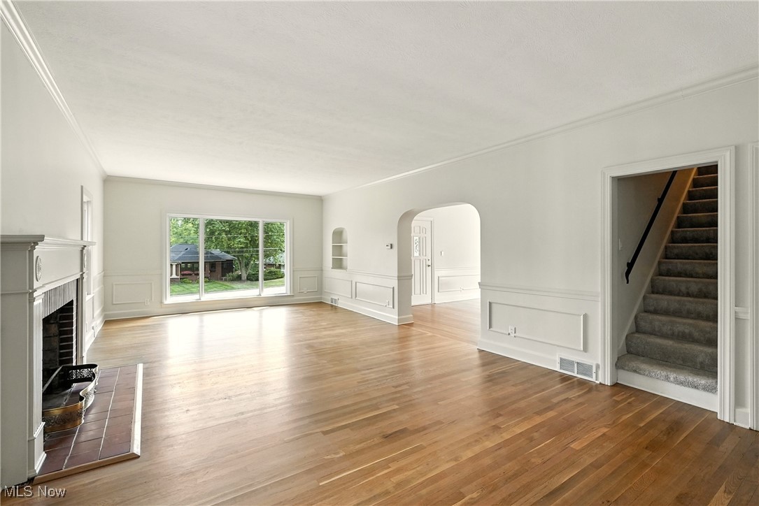 2844 Kent Road Stow, OH 44224 - Photo 21 of 47 Unfurnished living room featuring arched walkways, light wood-style flooring, a fireplace with raised hearth, stairway, and ornamental molding