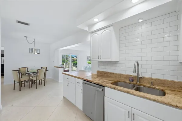a kitchen with stainless steel appliances granite countertop a stove top oven a sink a dining table and chairs with white cabinets