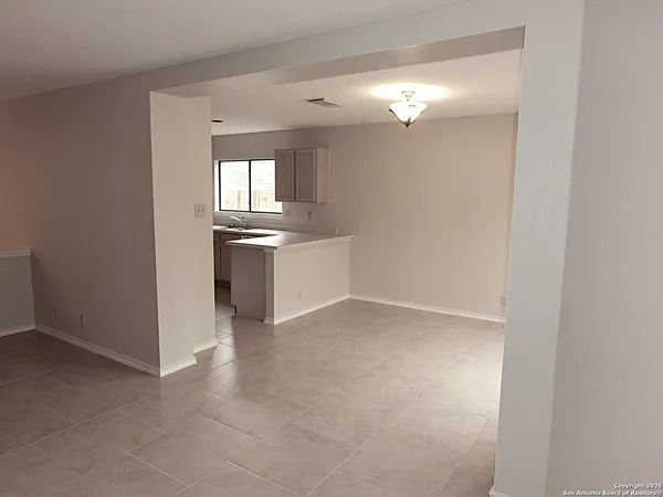 an empty room with chandelier fan and kitchen view
