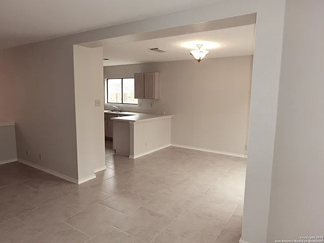 an empty room with chandelier fan and kitchen view