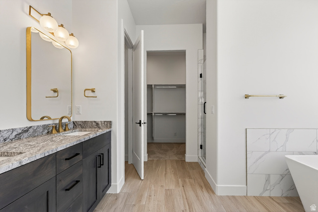 2862 South Mountain Rnch Road Cedar City, UT 84720 - Photo 24 of 64 Bathroom featuring a double vanity with stone countertops, a freestanding tub, a glass-enclosed shower, wood-finish flooring, and a walk-in closet
