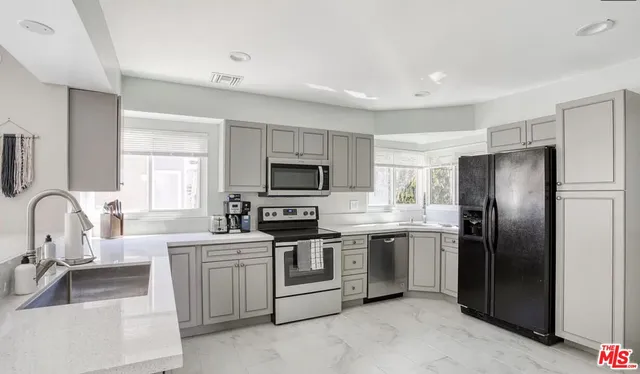 a kitchen with stainless steel appliances a sink a stove a refrigerator cabinets and a window