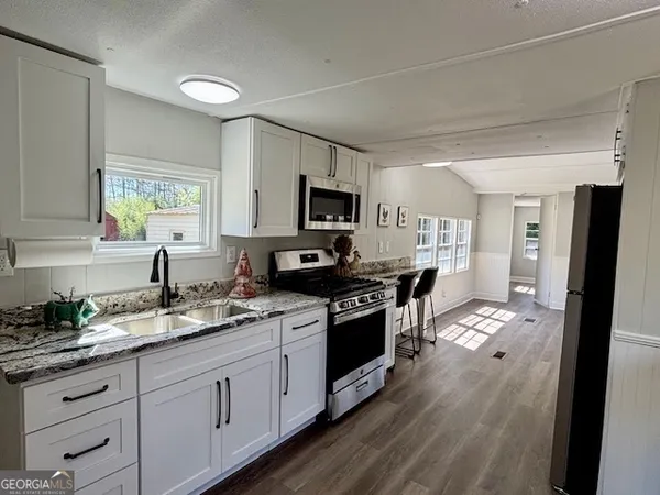 a kitchen with stainless steel appliances granite countertop a stove a sink dishwasher a refrigerator and a microwave oven with wooden floor