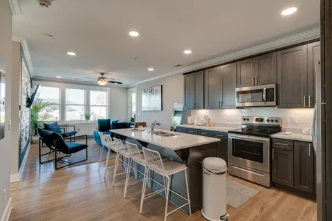 a kitchen with stainless steel appliances granite countertop a stove top oven a sink a dining table and chairs with wooden floor