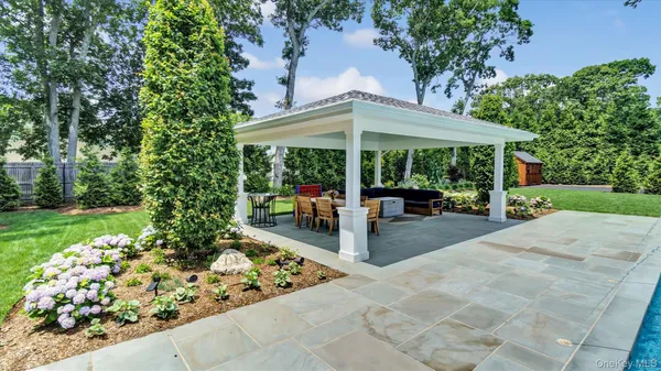 a view of a patio with table and chairs under an umbrella with large trees