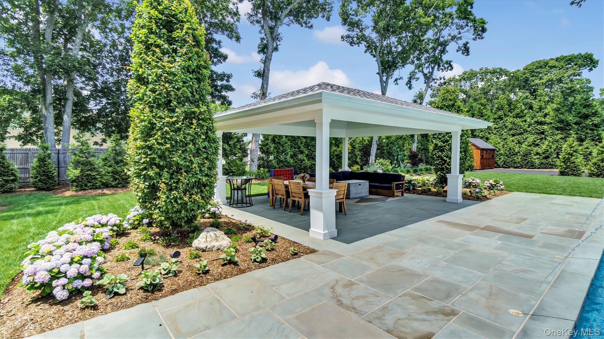 99 Beach Road Westhampton Beach, NY 11978 - Photo 33 of 37 a view of a patio with table and chairs under an umbrella with large trees
