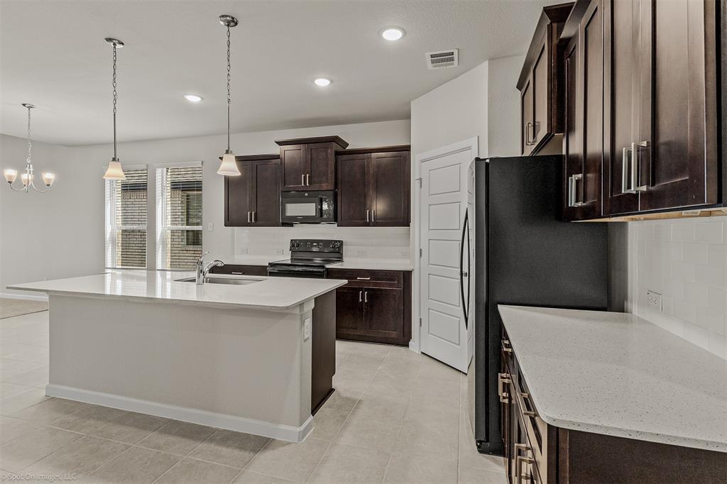 638 Pinehurst Road Red Oak, TX 75154 - Photo 35 of 38 Kitchen with dark wood finish cabinets, black appliances, a center island with sink, light stone countertops, and tasteful backsplash