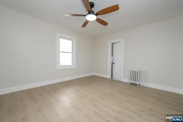 an empty room with wooden floor ceiling fan and windows