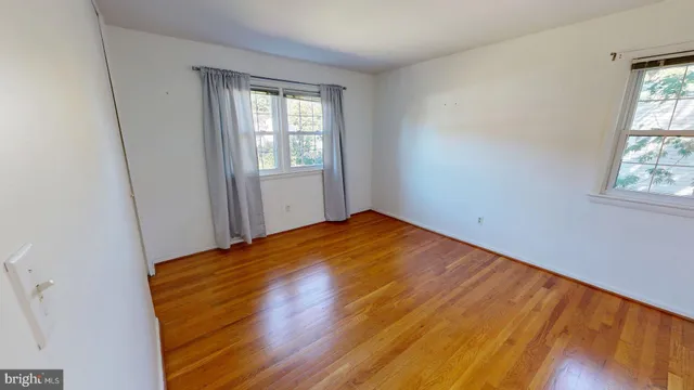 an empty room with wooden floor closet and windows