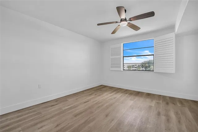 an empty room with wooden floor ceiling fan and windows
