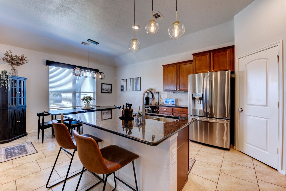 22939 Banff Brook Way Tomball, TX 77375 - Photo 9 of 25 Open-concept kitchen with breakfast bar seating, modern lighting, and seamless flow into the dining and living spaces—ideal for everyday living and entertaining.