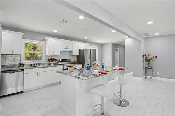 a kitchen with stainless steel appliances kitchen island granite countertop a stove a sink a dining table and chairs