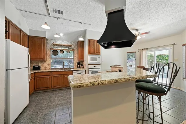 a kitchen with granite countertop a refrigerator a stove a dining table and chairs with wooden floor