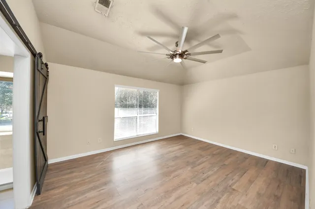 an empty room with wooden floor fan and windows
