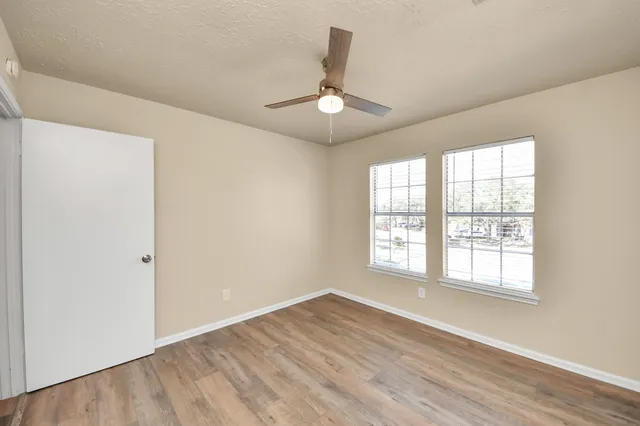 an empty room with wooden floor chandelier fan and windows
