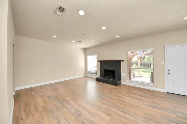 an empty room with wooden floor fireplace and windows