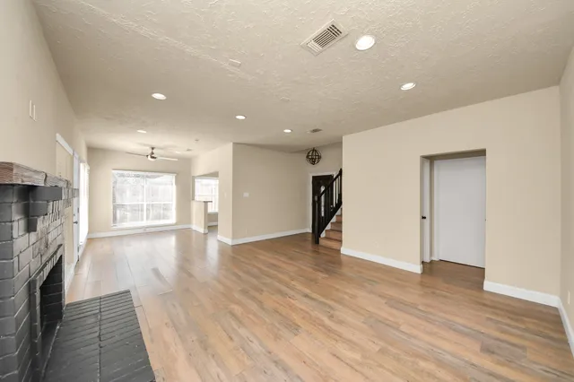 a view of an empty room with wooden floor and a kitchen